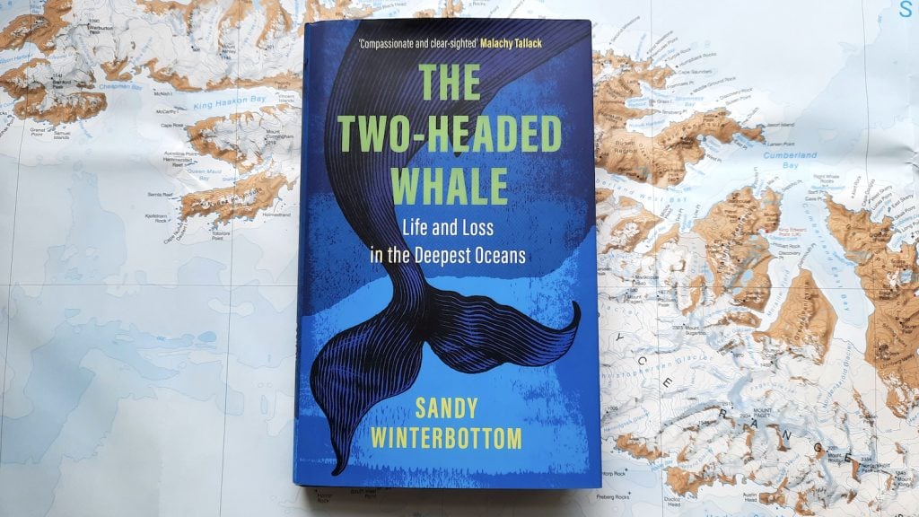 A copy of 'The Two-Headed Whale' by Sandy Winterbottom. The book sits on a background of the map of South Georgia