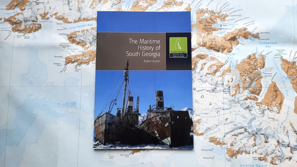 A copy of the book 'The Maritime History of South Georgia' by Robert Burton, published by the South Georgia Heritage Trust. he book sits on a background of the map of South Georgia.