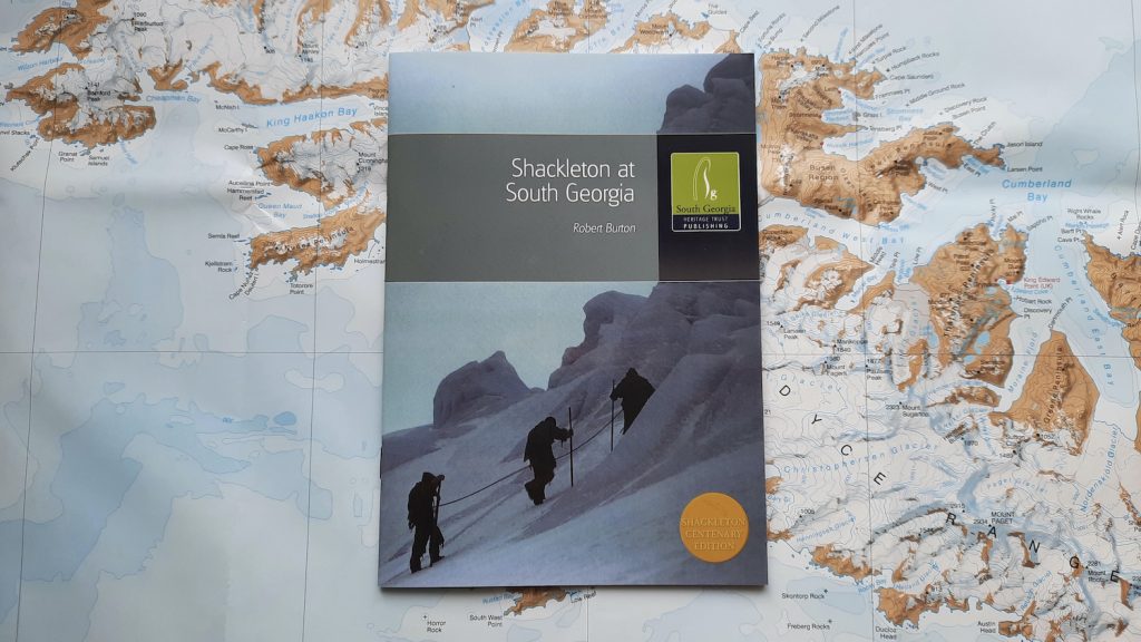 A copy of the book 'Shackleton at South Georgia' by Robert Burton, published by the South Georgia Heritage Trust. he book sits on a background of the map of South Georgia.