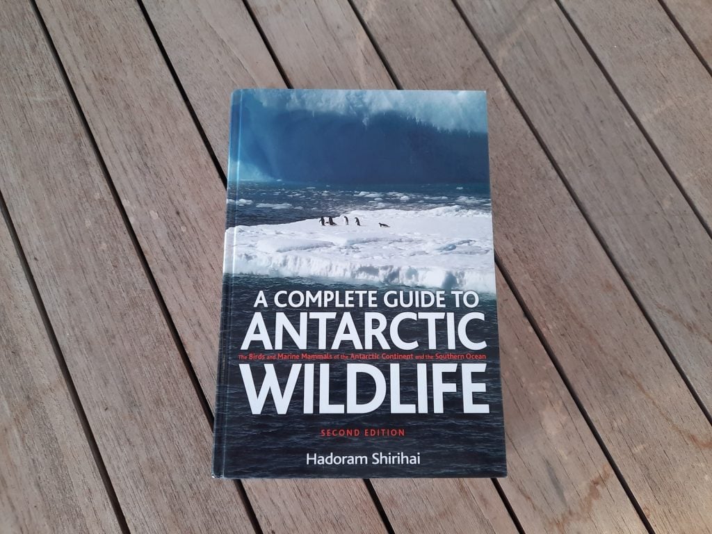 A copy of A Complete Guide to Antarctic Wildlife by Hadoram Shirihai on the decking of a cruise ship. There are penguins on an iceberg on the cover.