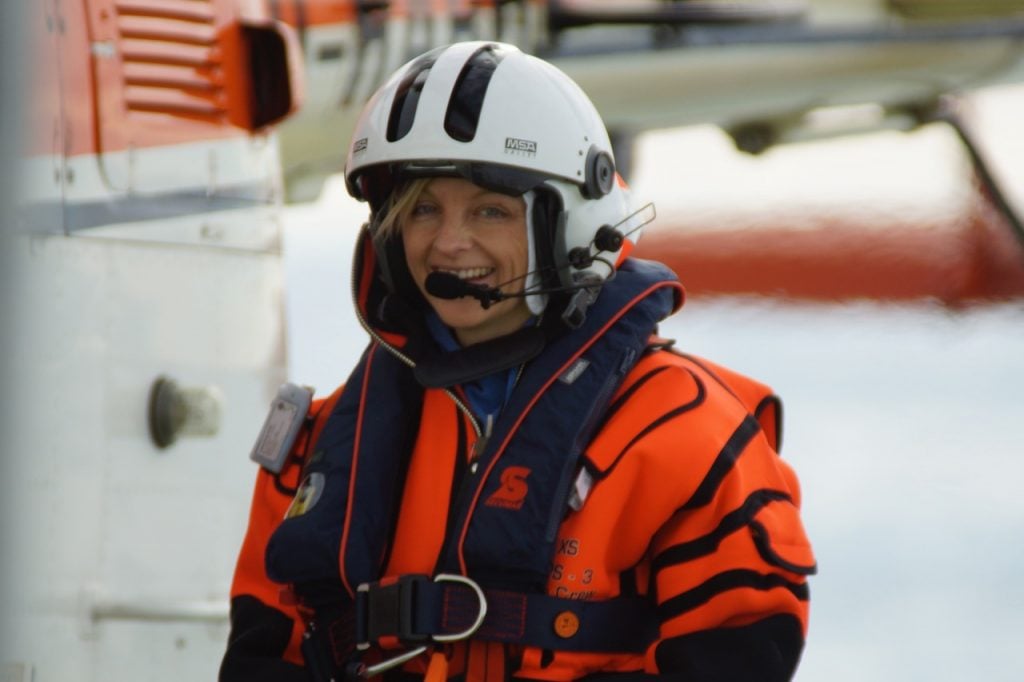 Dr Helena Herr in orange gear, life jacket and helmet standing front of a helicopter on the Research Vessel Polarstern. The photo credit is Carsten Rochol
