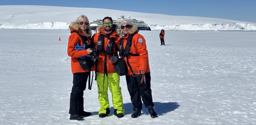 Three tourists on the pack ice in Antarctica with an expedition cruise ship behind them