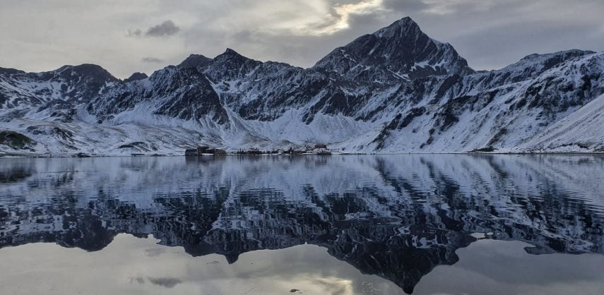 Snowy mountains over Grytviken in South Georgia, reflected in the waters of Cumberland Bay