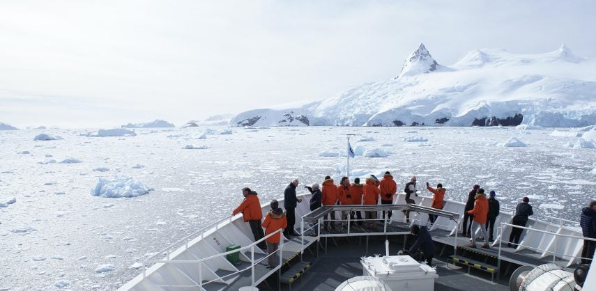 Passengers at the bow of an Antarctic cruise ship, with an icy sea and mountains